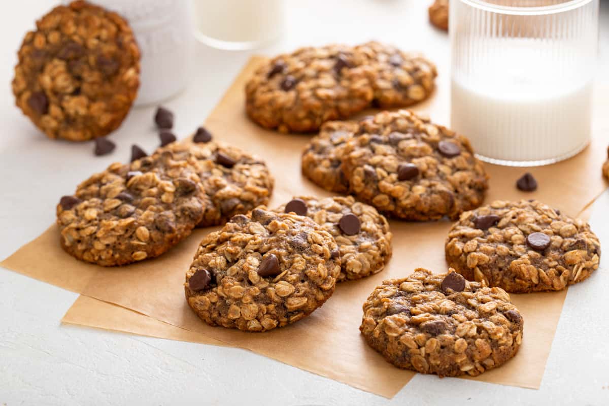 Banana oatmeal cookies scattered on pieces of parchment paper. A glass of milk is in the background.