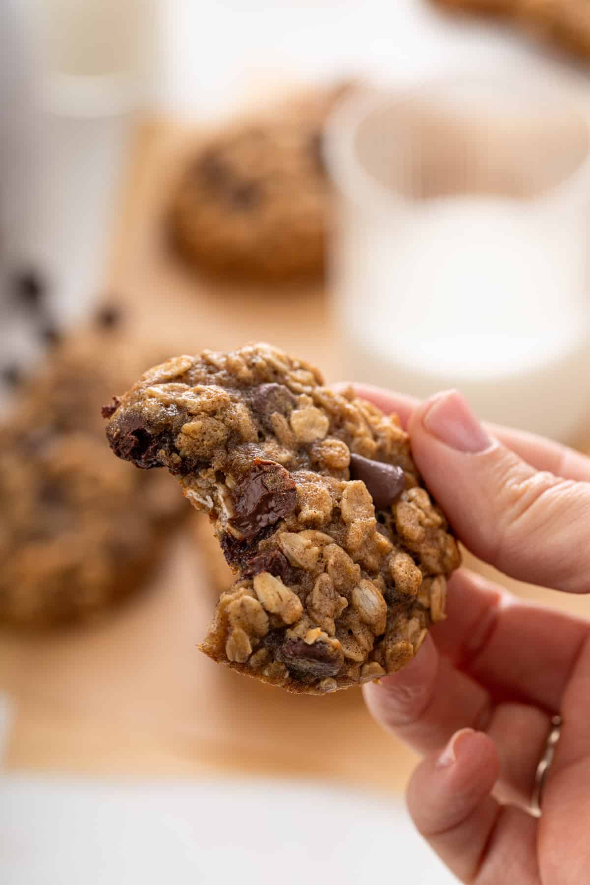 Hand holding up a banana oatmeal cookie with a bite taken from it.