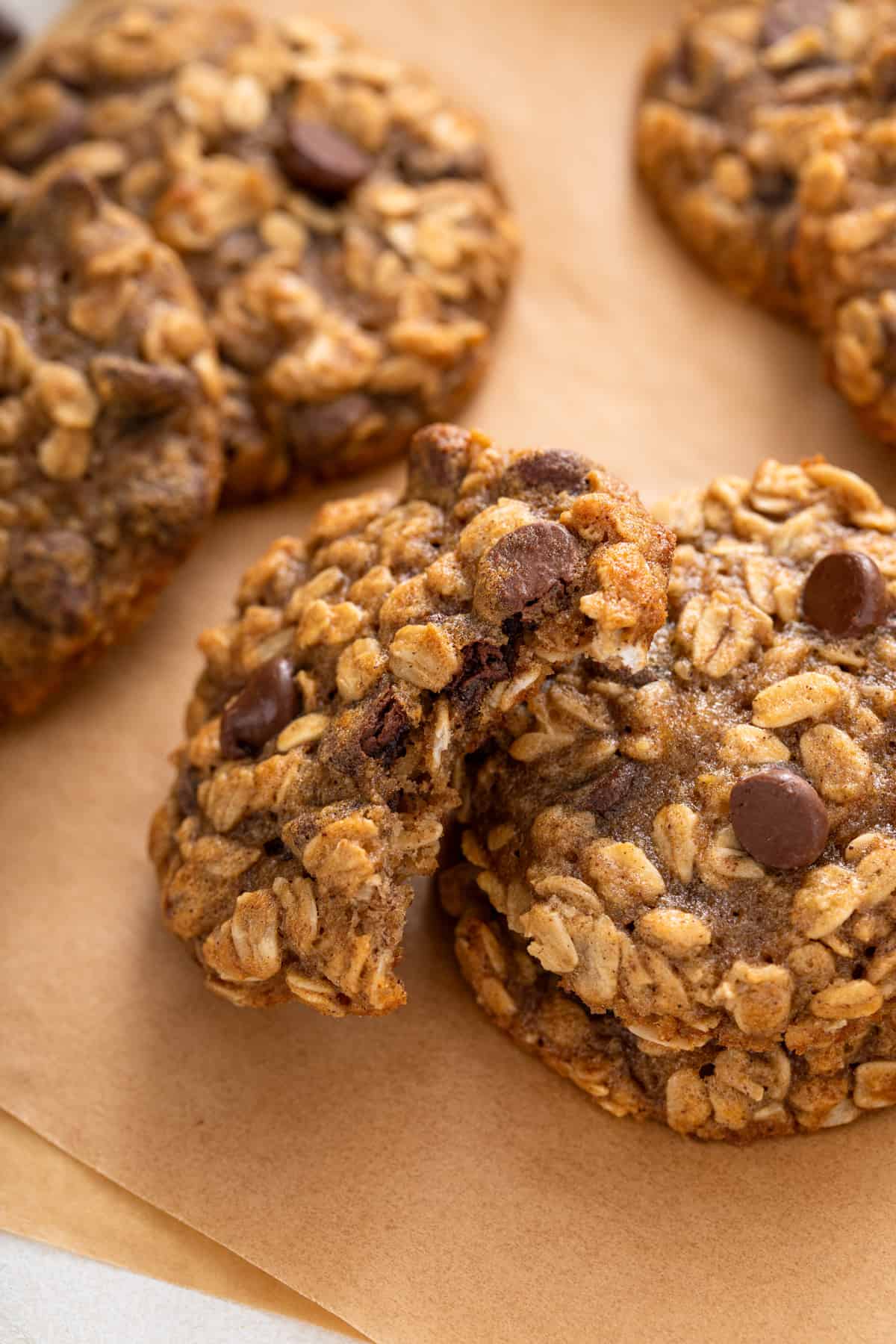 Halved banana oatmeal cookie propped against two stacked cookies on a piece of parchment paper.