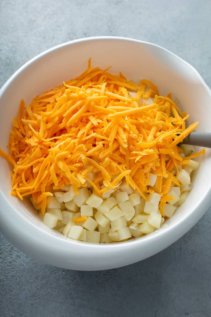 Spatula adding diced hash brown potatoes and shredded cheese to a white bowl