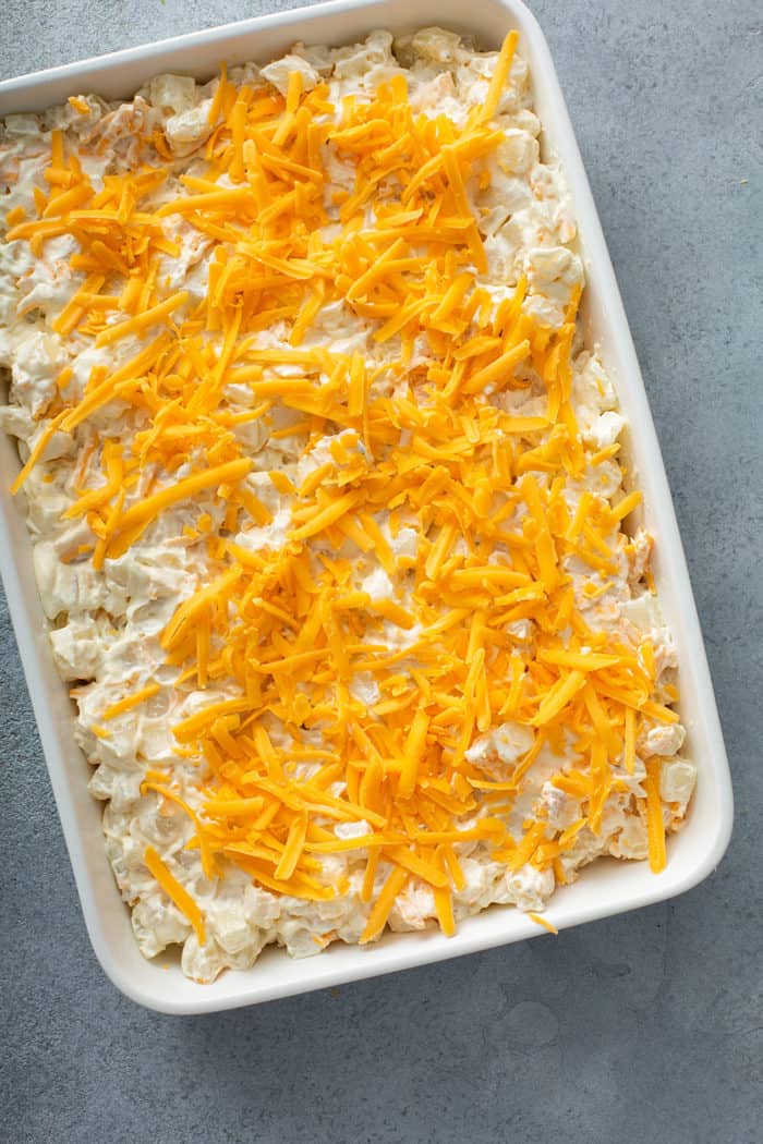 Unbaked hash brown casserole topped with shredded cheese in a white baking dish