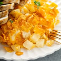 Close up of hash brown casserole on a white plate next to sliced chicken breast