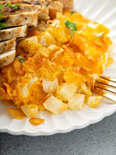 Close up of hash brown casserole on a white plate next to sliced chicken breast