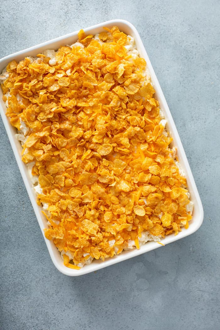 Unbaked hash brown casserole in a white baking dish, topped with corn flakes