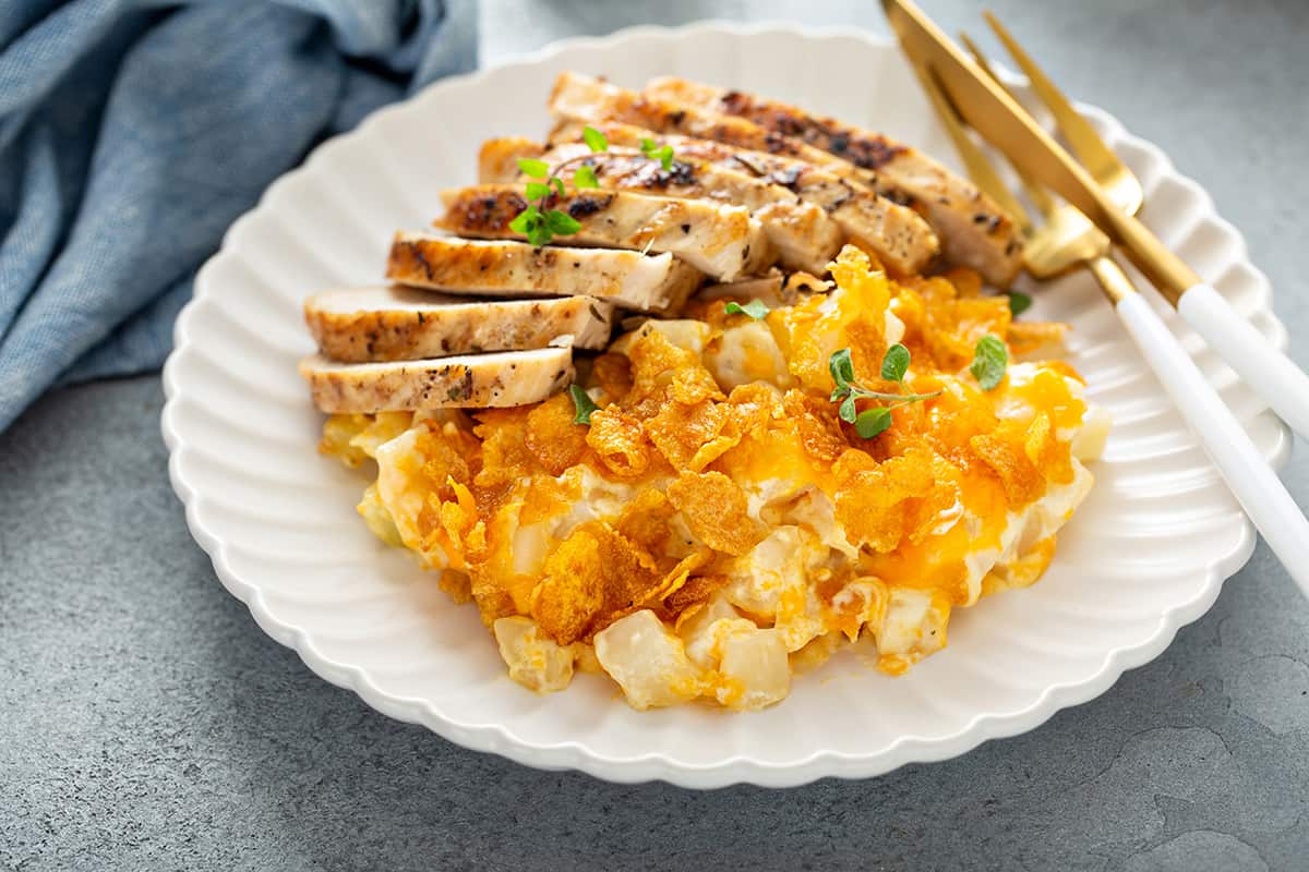 Plated hash brown casserole on a white plate alongside sliced chicken breast