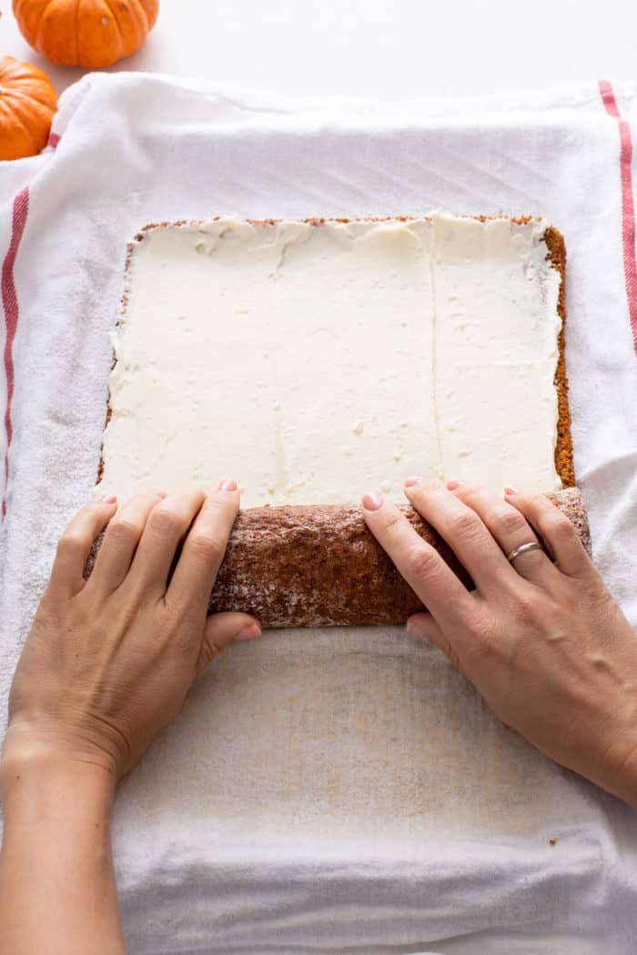 Hands rolling pumpkin roll with cream cheese filling.