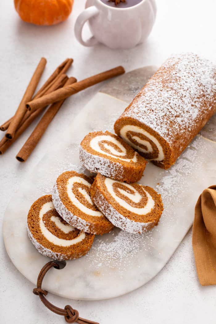 Pumpkin roll dusted with powdered sugar and sliced on a marble board.
