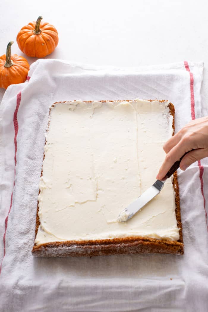 Cream cheese filling being spread into an unrolled pumpkin sponge.