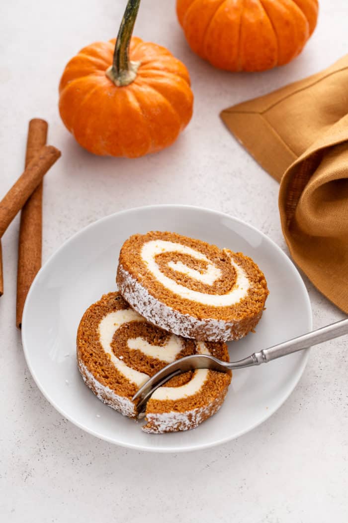 Fork cutting a bite from a slice of pumpkin roll on a plate.