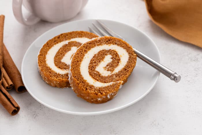 Two slices of pumpkin roll next to a fork on a white plate.