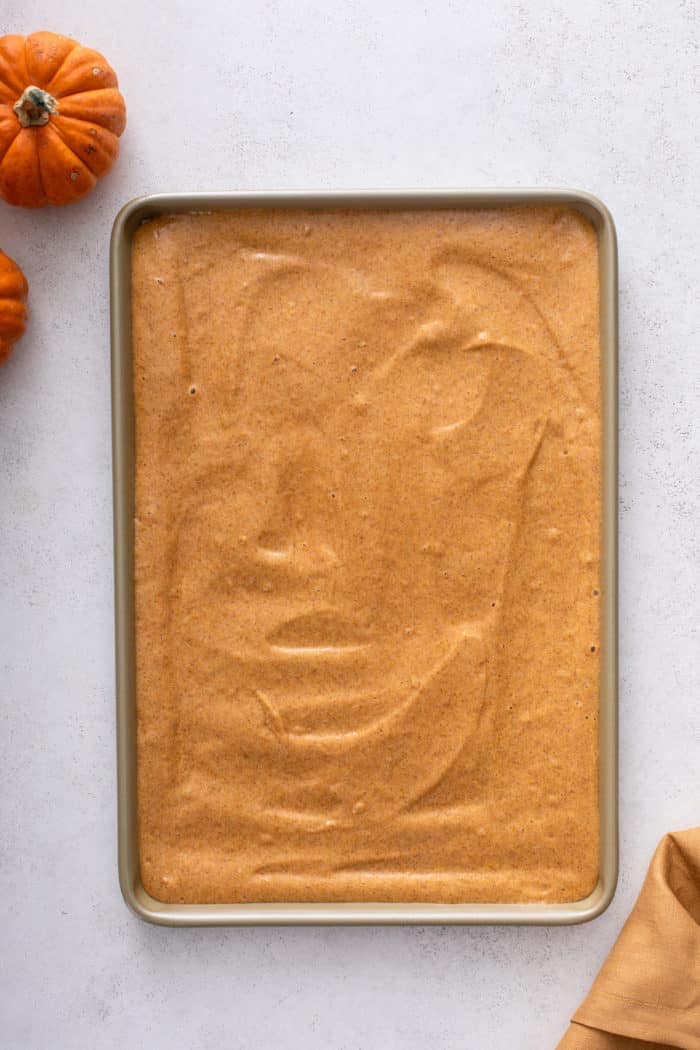 Batter for pumpkin roll spread into a jelly roll pan, ready to go in the oven.