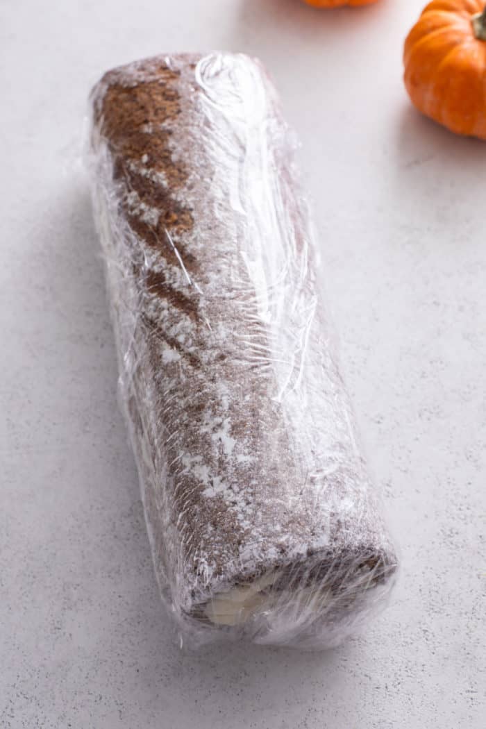 Rolled pumpkin roll wrapped in plastic wrap.