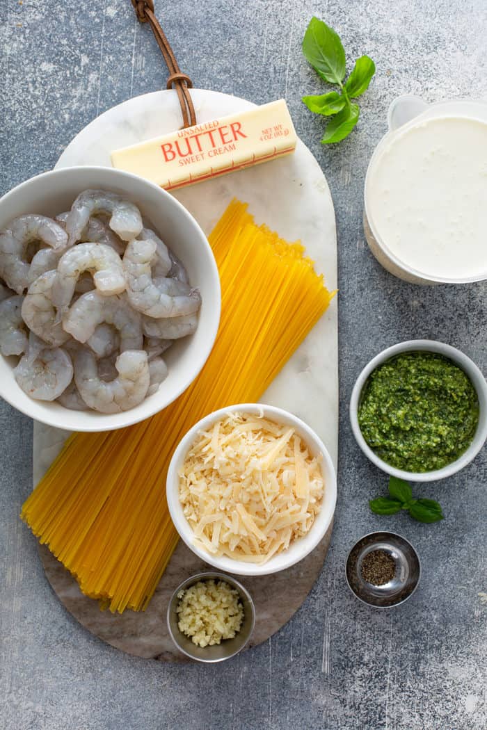 Ingredients for creamy pesto pasta with shrimp on a gray counter