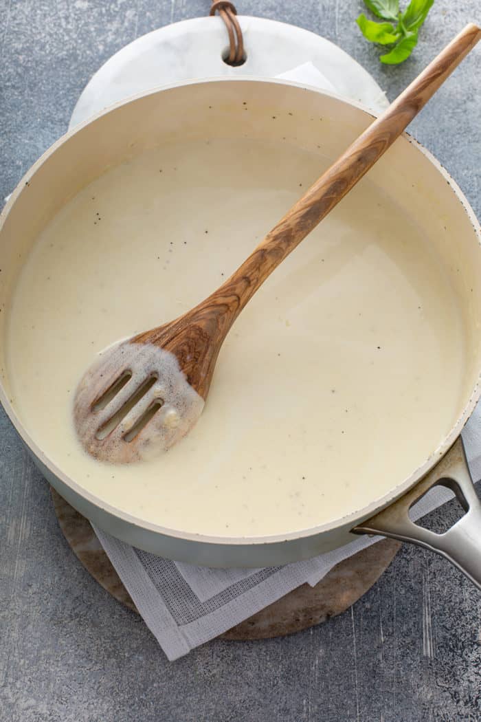 Spoon stirring together the creamy alfredo base of creamy pesto pasta sauce in a saucepan