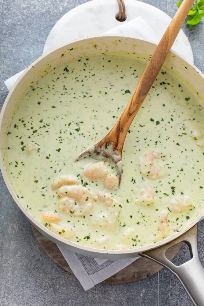 Spoon stirring creamy pesto pasta sauce with shrimp in a shallow saucepan