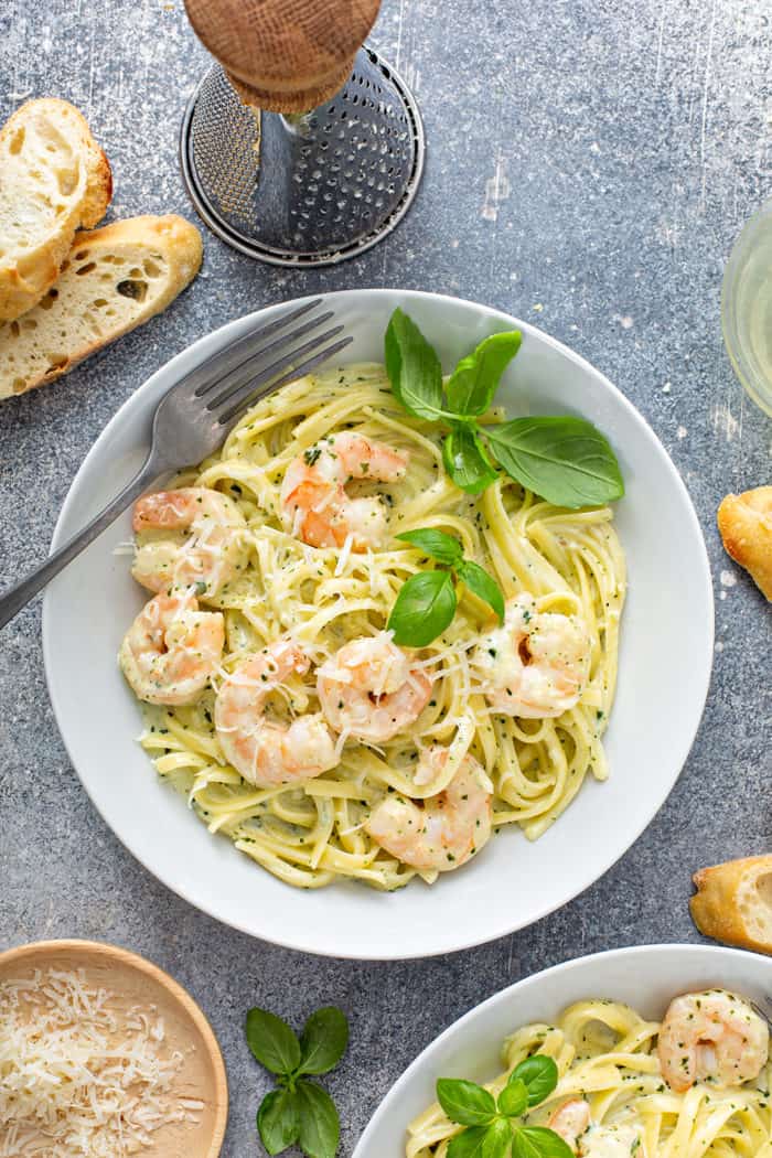 Overhead view of a fork set in a bowl of creamy pesto pasta with shrimp, garnished with fresh basil