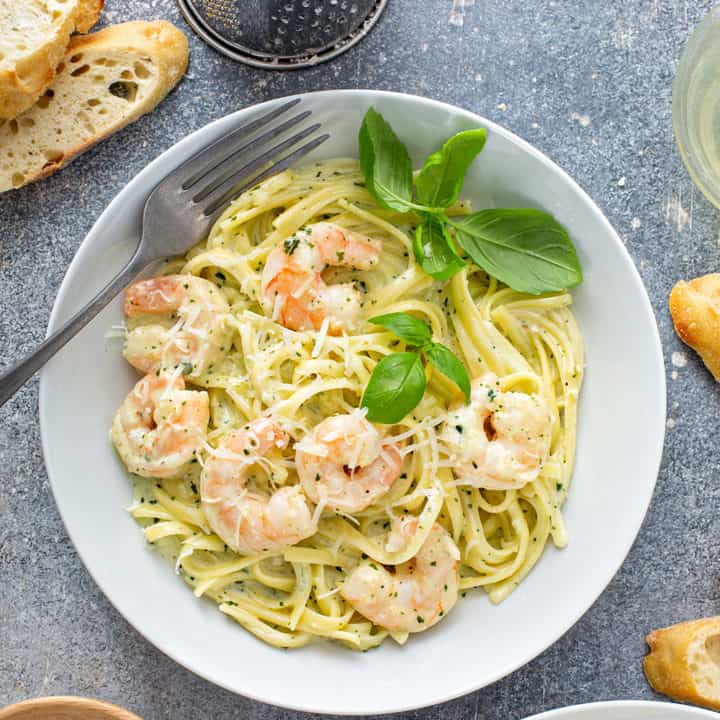 Overhead view of a fork set in a bowl of creamy pesto pasta with shrimp, garnished with fresh basil