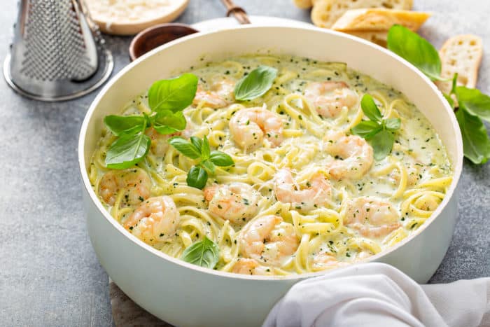 Wide, shallow sauce pot filled with creamy pesto pasta with shrimp set on a gray countertop