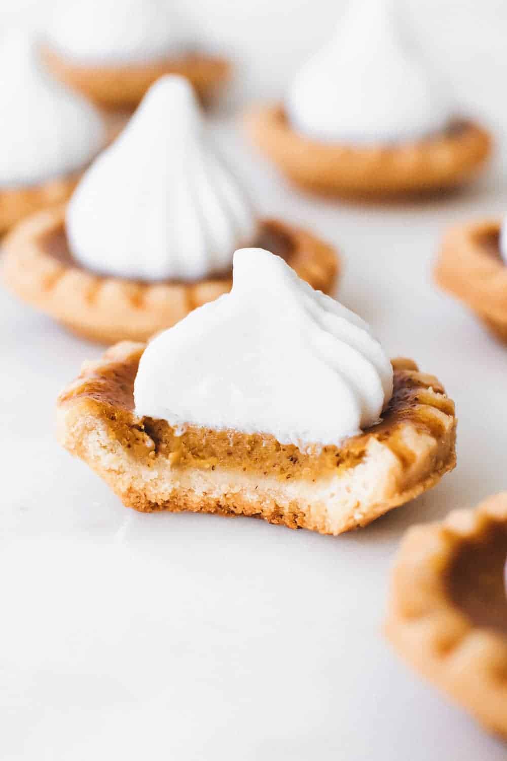 Close up of a mini pumpkin pie topped with whipped cream with a bite taken out of it
