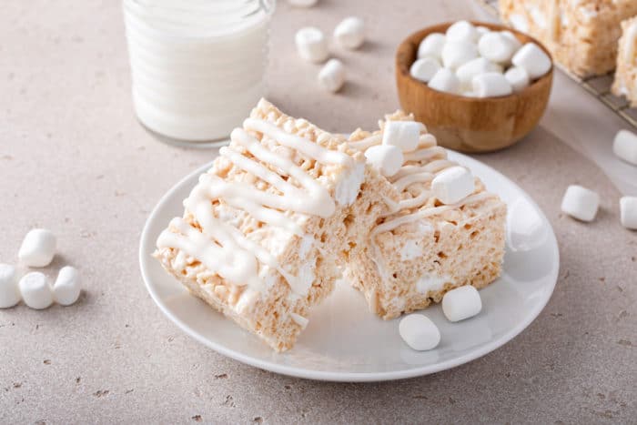 Two brown butter rice krispie treats arranged on a white plate with a glass of milk in the background.