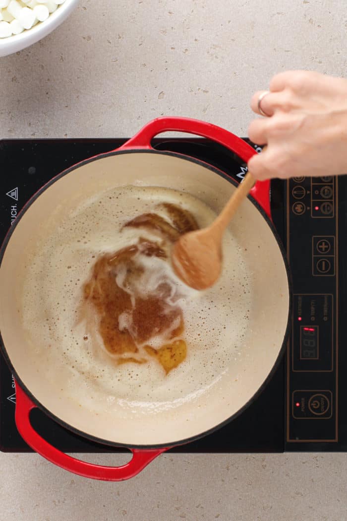 Stirring brown butter with a wooden spoon in a large dutch oven.