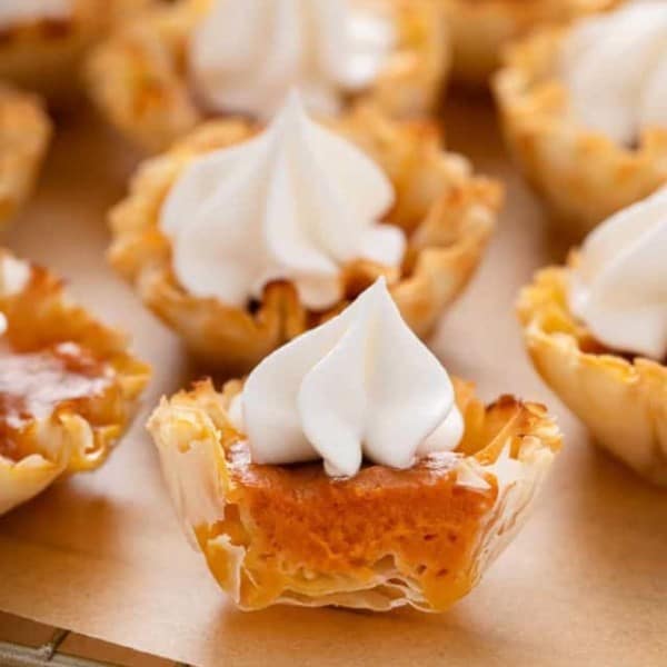 Halved mini pumpkin pie topped with whipped cream on a wire rack.