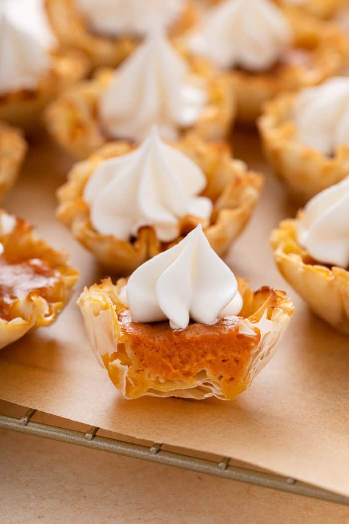 Halved mini pumpkin pie topped with whipped cream on a wire rack.