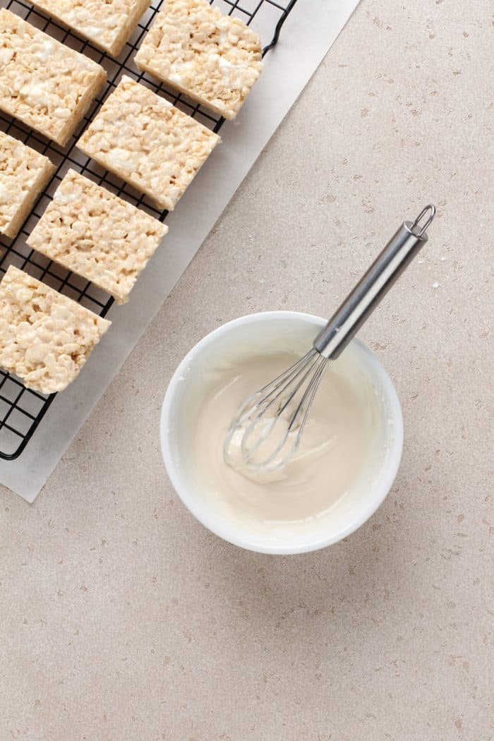 Maple icing for brown butter rice krispie treats in a small white bowl next to cooled krispie treats.