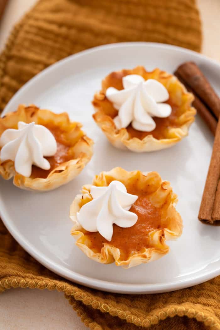 Three mini pumpkin pies garnished with whipped cream on a white plate.