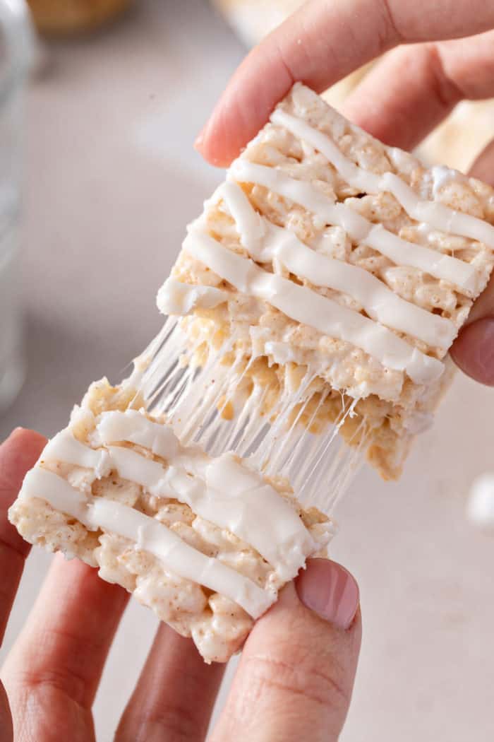 Hand pulling apart the two halves of an iced brown butter rice krispie treat.