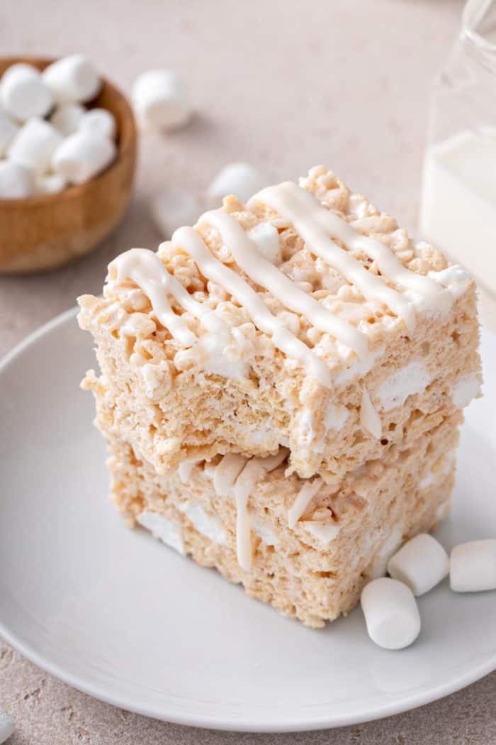 Two brown butter rice krispie treats stacked on a white plate. The top treat has a bite taken out of the corner.