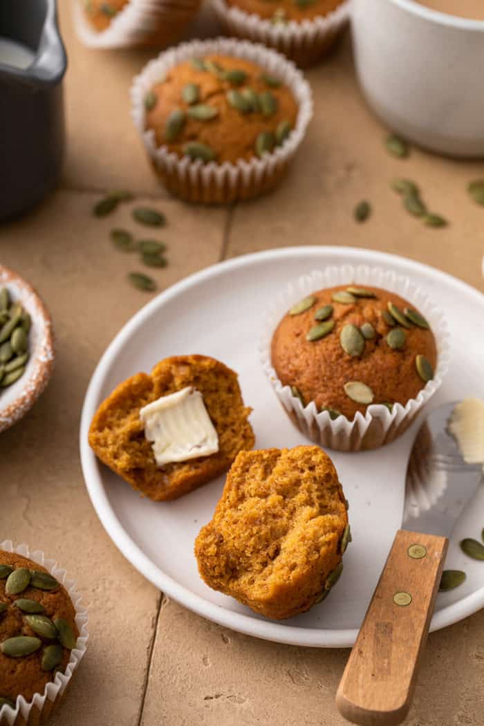 Two pumpkin muffins on a white plate. One muffin is split in half with butter on one half
