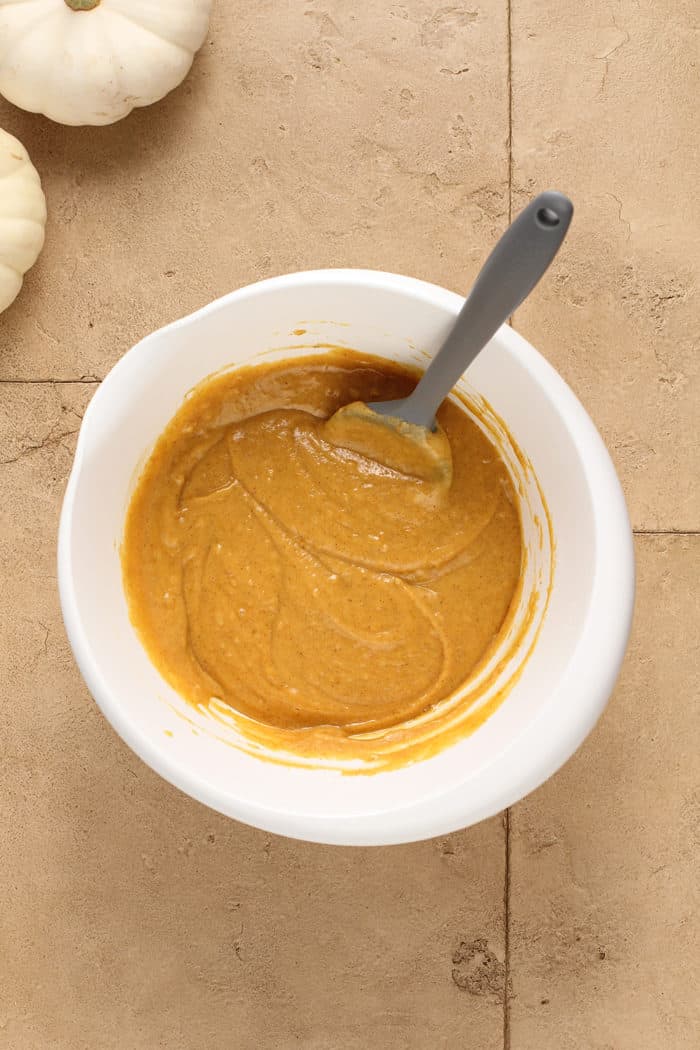 Spatula stirring together pumpkin muffin batter in a white mixing bowl