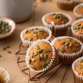 Pumpkin muffins topped with pumpkin seeds on a wire rack