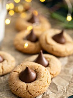 Peanut butter blossoms arranged on a piece of parchment paper, with christmas lights twinkling in the background
