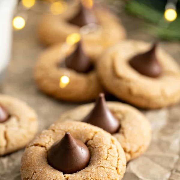 Peanut butter blossoms arranged on a piece of parchment paper, with christmas lights twinkling in the background