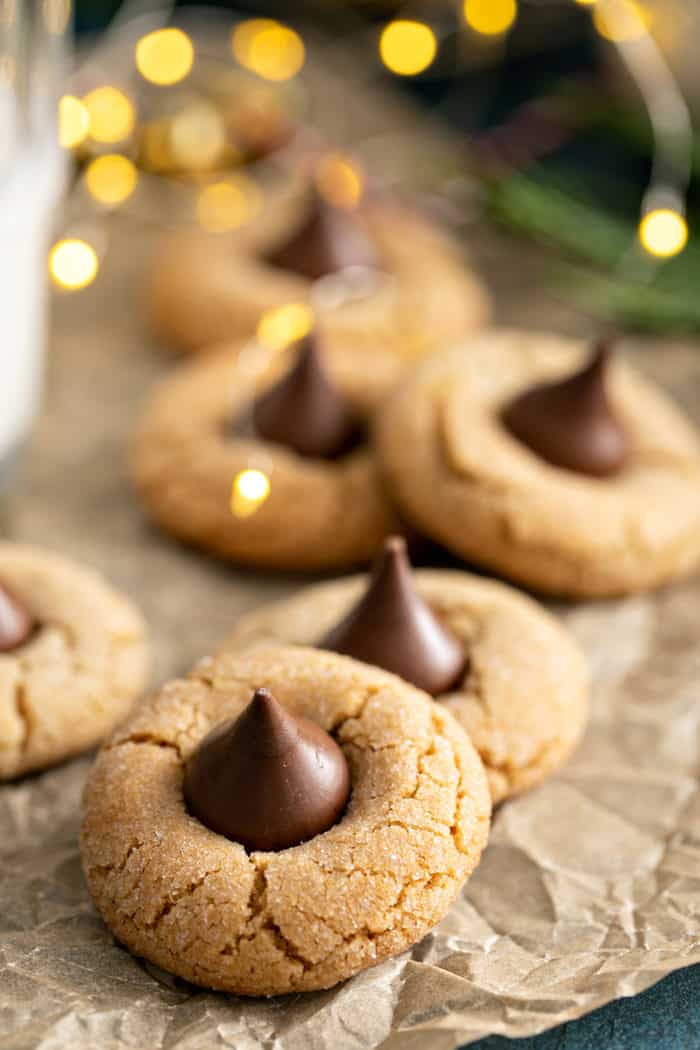 Peanut butter blossoms arranged on a piece of parchment paper, with christmas lights twinkling in the background