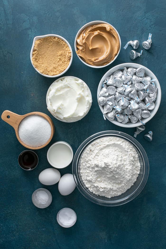Ingredients for peanut butter blossom cookies arranged on a blue countertop