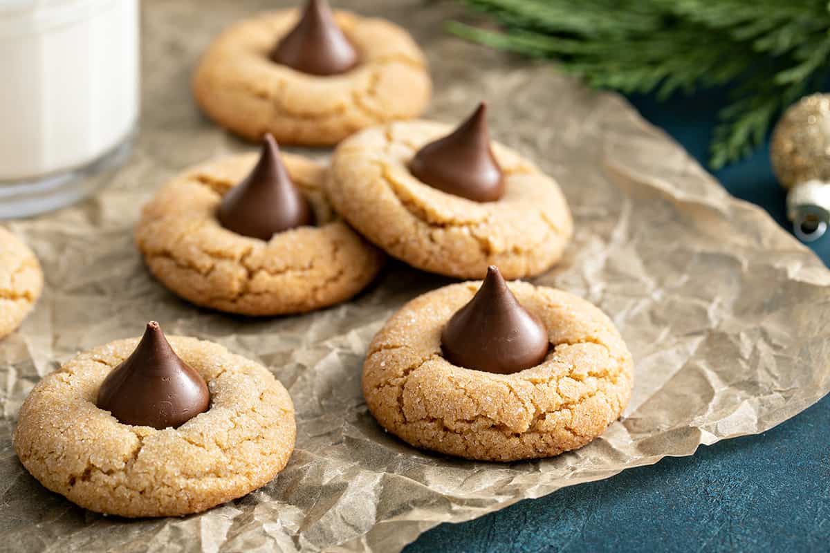 Peanut butter blossom cookies arranged on a piece of parchment paper next to a glass of milk