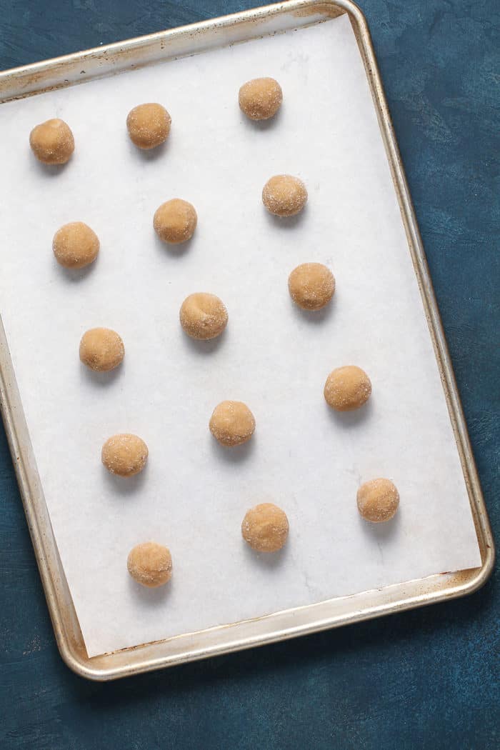 Balls of peanut butter blossom dough arranged on a parchment-lined baking sheet, ready to bake