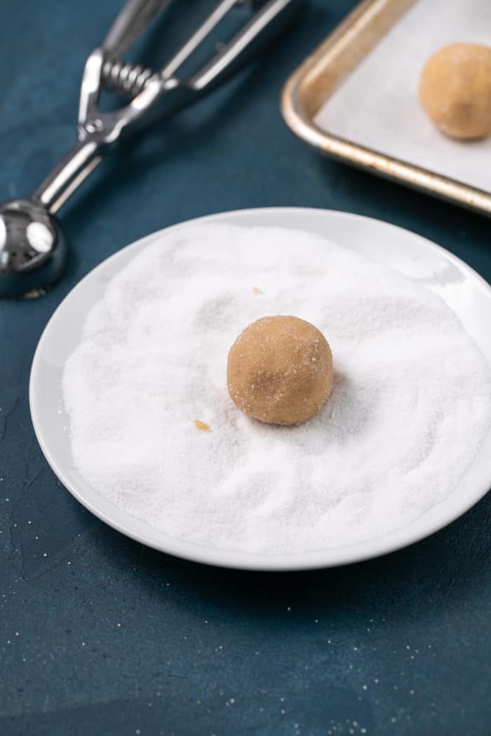 Ball of peanut butter blossom cookie dough being rolled in granulated sugar
