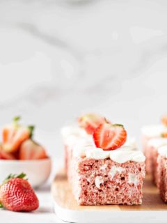 Side view of a strawberry rice krispie treat on a wooden cutting board next to a fresh strawberry