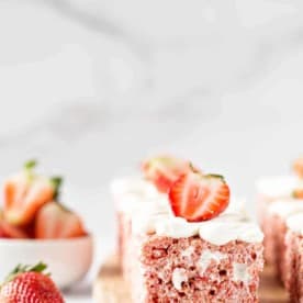 Side view of a strawberry rice krispie treat on a wooden cutting board next to a fresh strawberry