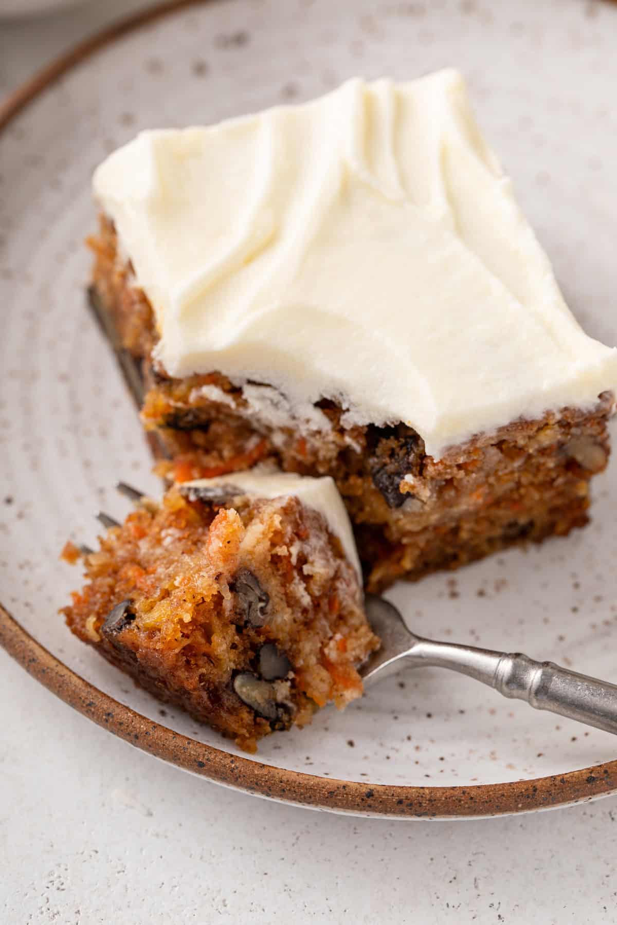 Fork cutting a corner off a slice of j alexander's carrot cake on a plate.