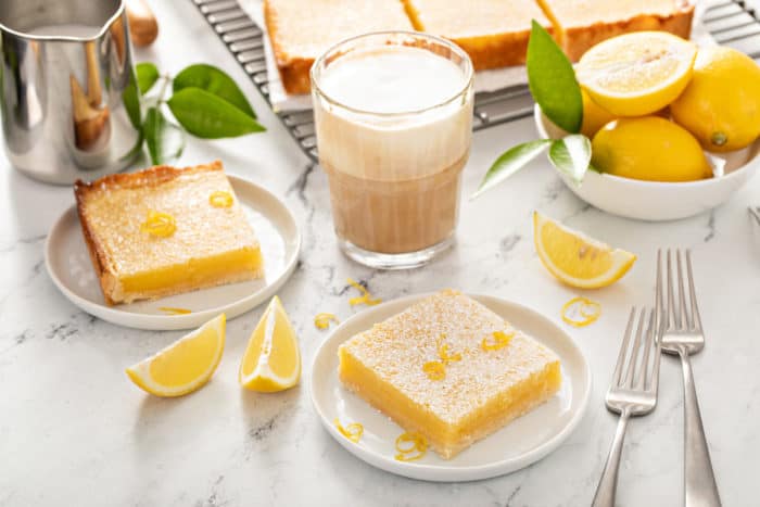 Two lemon bars on white plates on a marble countertop.