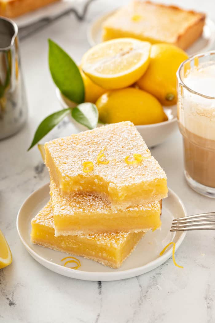 Three stacked lemon bars on a white plate, with a bite taken out of the corner of the top bar.