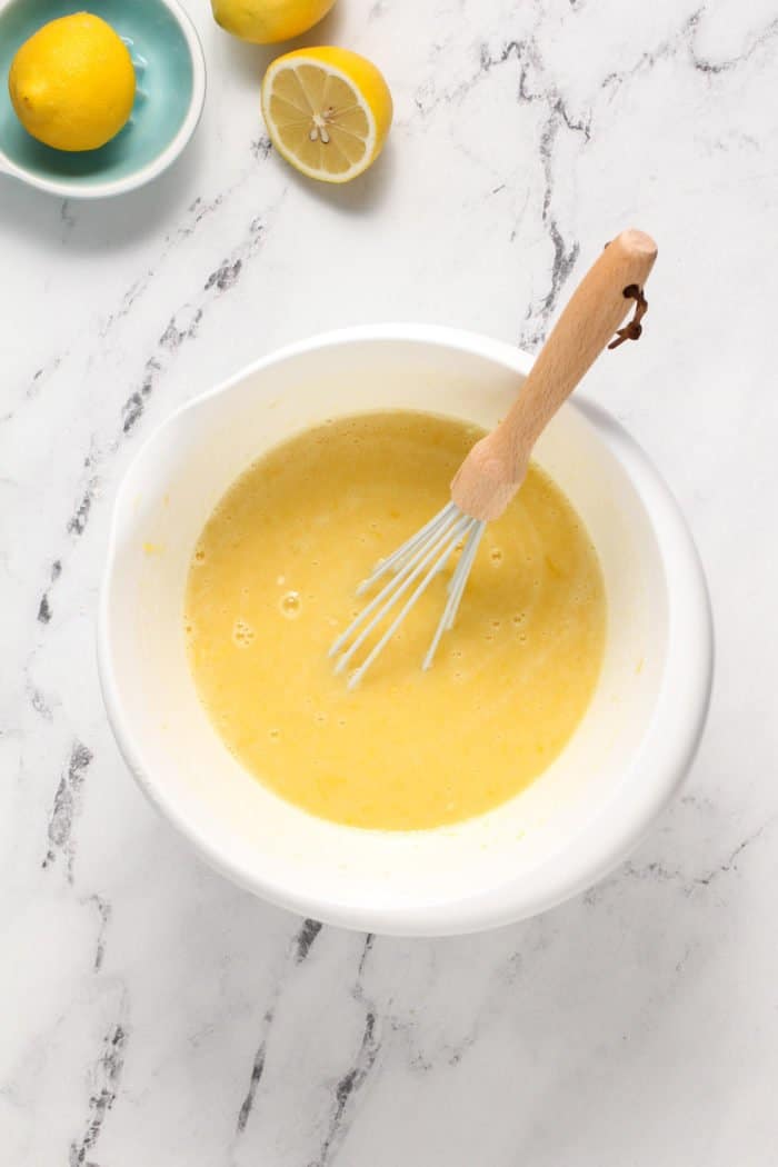 Lemon filling for lemon bars being whisked in a white bowl.