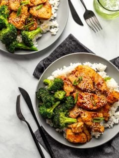 Two plates of honey soy chicken served with rice and broccoli