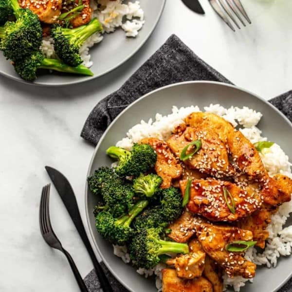 Two plates of honey soy chicken served with rice and broccoli