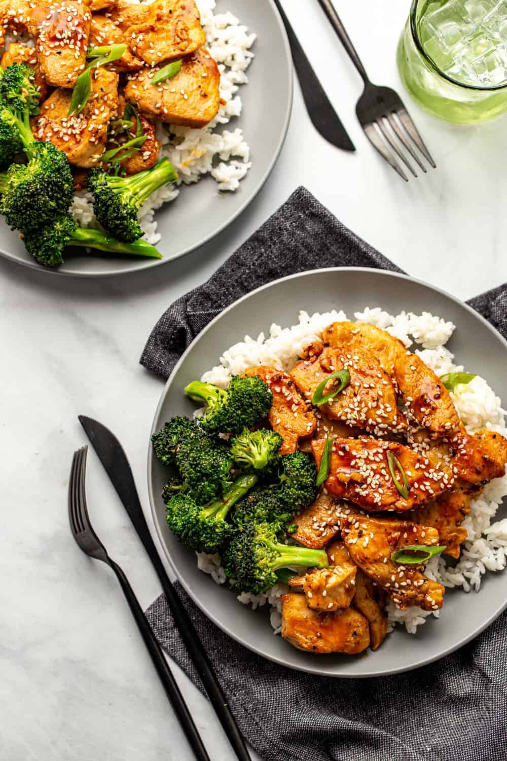 Two plates of honey soy chicken served with rice and broccoli